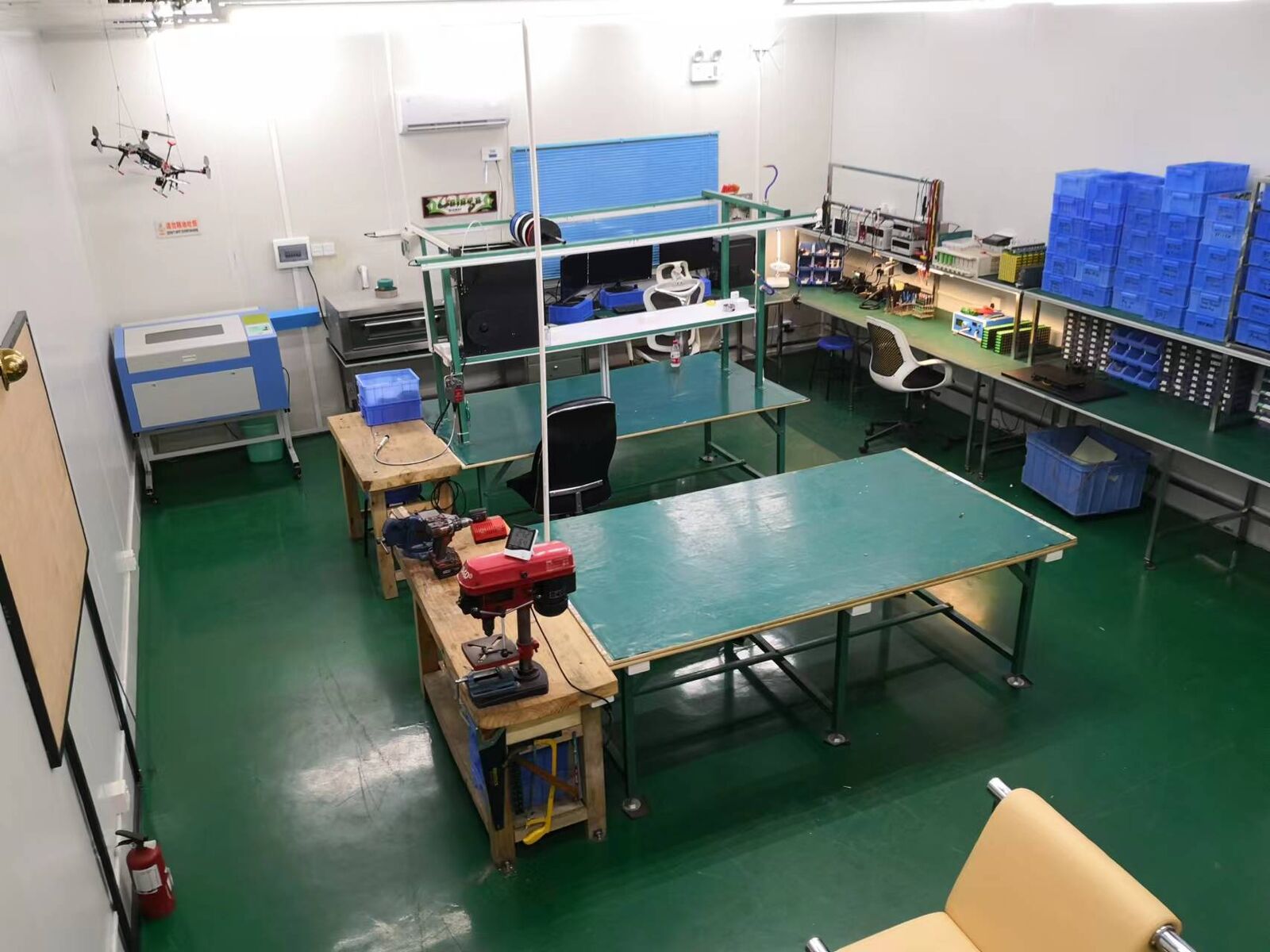 Interior of a small assembly and test workshop with green floor, benches and a laser cutter.