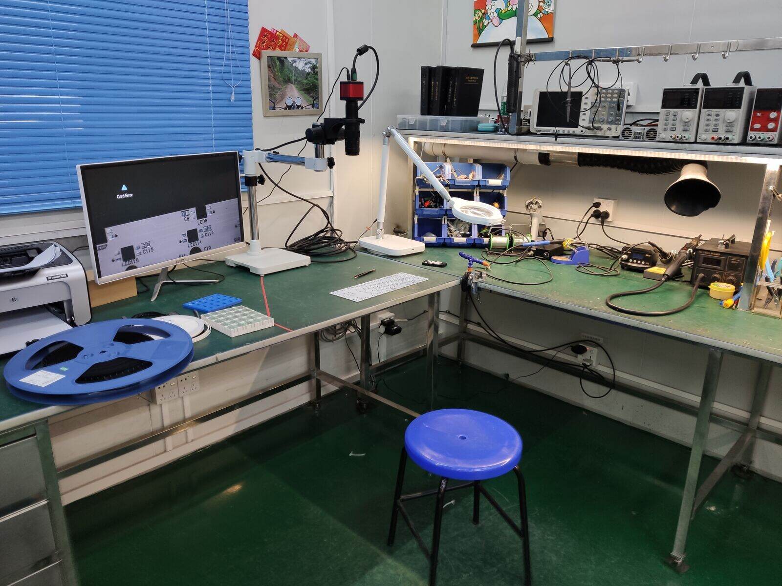 A small Chinese electronics workshop with benches, tools and blue parts bins.