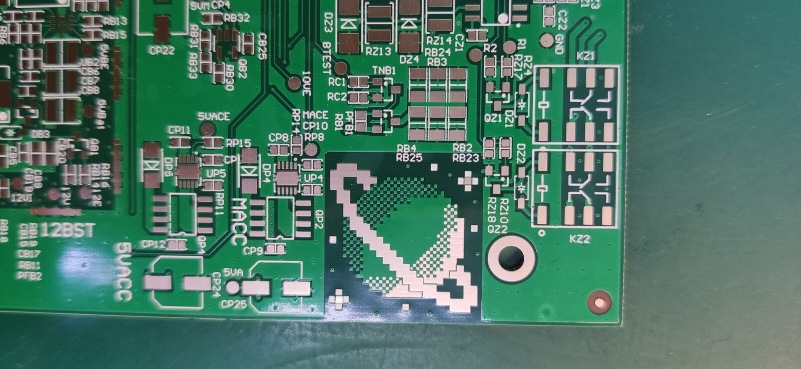 Close-up of a green circuit board with a pixel-art planet-like logo among small components.