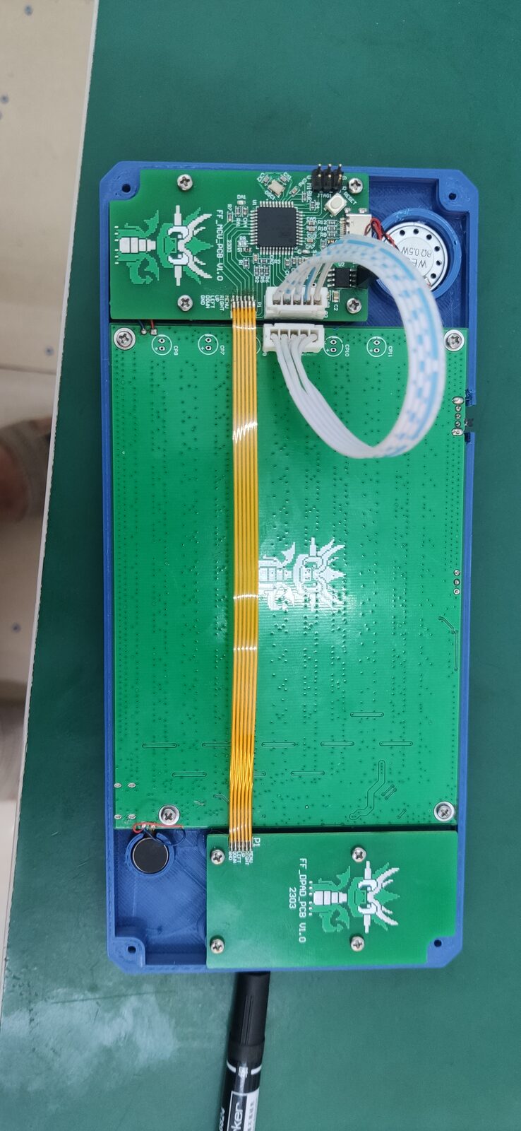 Opened handheld on a green mat showing green circuit boards joined by a flat ribbon cable.