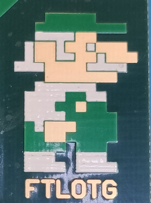 Close-up of a green circuit board with copper and soldermask pixel art of a running figure in a green cap, with FTLOTG below.